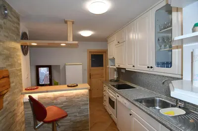 a kitchen with white cabinets and a sink and a chair at Apartment Perunika in Cerkno