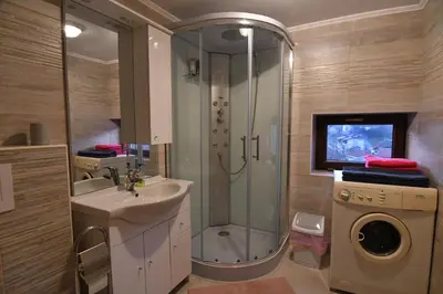 a bathroom with a shower and a sink and a washing machine at Apartment Perunika in Cerkno