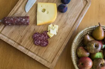 a wooden cutting board with cheese and a basket of fruit at Vila Labod, unique villa at the lake in Most na Soči