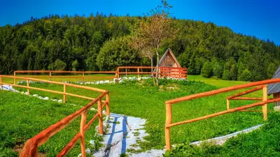 a wooden fence in a field with a barn at Glamping Vrhovc in Železniki