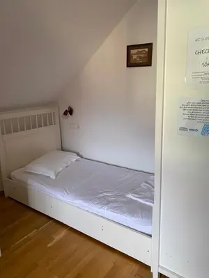 a small bed in a room with a white wall at Travellers' Haven Hostel in Bled