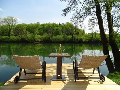 two chairs and a table with wine glasses on a dock next to a lake at Kolpa Paradise in Metlika