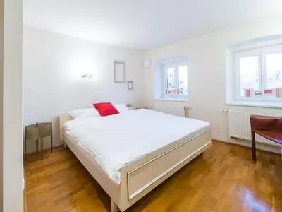 a white bedroom with a large white bed with a red pillow at Stairway to the castle in Ljubljana