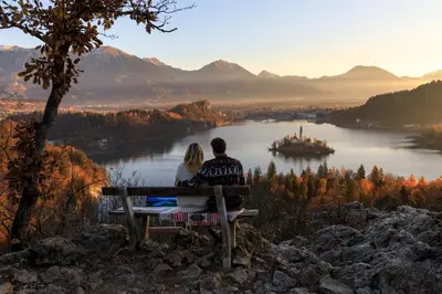 a man and woman sitting on a bench overlooking a lake at Apartment Mavrica Bled, quiet location, with a view of the lake in Bled