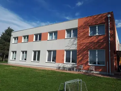 a building with chairs and a soccer field in front of it at Penzion Letališče in Murska Sobota