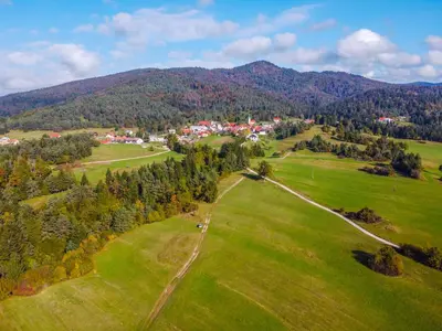 an aerial view of a green field with a town and mountains at Notranjska hiša - traditional country house, close to the world attraction Cerknica lake in Begunje pri Cerknici