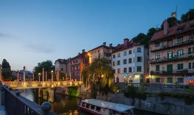 a bridge over a river with buildings and a boat at Kollmann Rooms and Apartments in Ljubljana