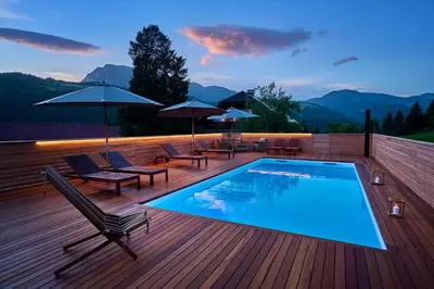 a swimming pool on a wooden deck with chairs and umbrellas at Domačija Metul in Luče