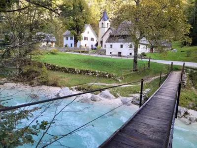 a bridge over a river in front of a house at Počitniško stanovanje Pri cerkvi in Trenta