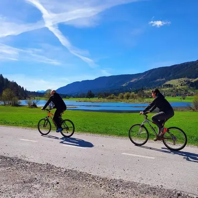 two men riding bikes on a road near a lake at Villa Nebina in Rateče