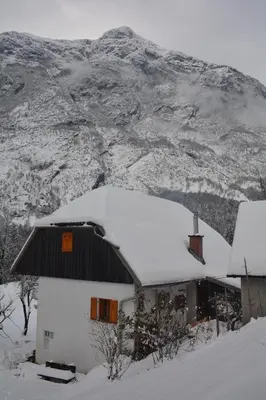 a house covered in snow in front of a mountain at Rustic Apartment PETRA in Soča