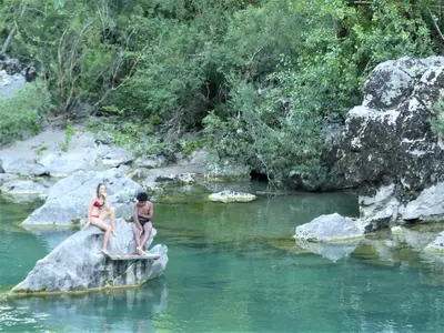 two people sitting on a rock in a river at Hiša ob potoku in Avče