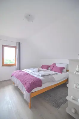 a white bedroom with a bed with purple pillows at Flower house Podčetrtek in Podčetrtek