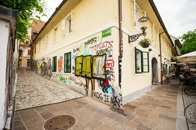 a street with graffiti on the side of a building at 150 steps to the main square in Ljubljana