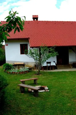 a building with a red roof and a bench in the grass at Balajceva domačija - Moravske Toplice in Moravske Toplice