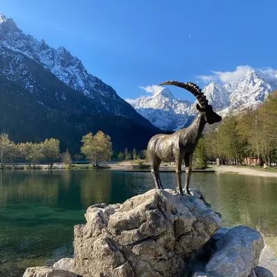 a statue of a ram standing on a rock near a lake at Pri Marusi in Kranjska Gora