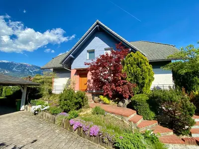 a blue house with a red door and some bushes at House Eden with Mountain Views in Bled