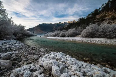 a river with snow covered rocks next to a mountain at Apartmaji Prton Bovec in Bovec