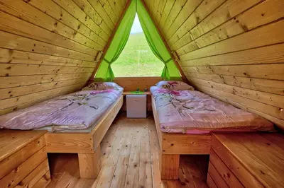two beds in a wooden room with a window at Glamping Brodej in Vitanje