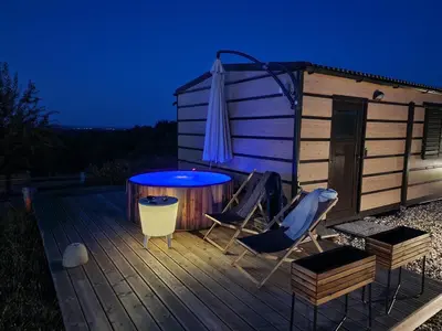 a deck with a hot tub and two chairs and an umbrella at VINEA PANONIKA wine & mind retreat in Radenci