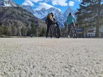 two people riding bikes on a road with mountains in the background at Koča Martuljek in Gozd Martuljek