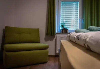 a bedroom with a green chair and a window at Hiša Bohinc z wellnessom in Tolmin