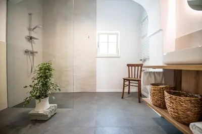 a bathroom with a glass shower and a chair at MEŽNARIJA Radovljica in Radovljica