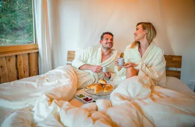 a man and woman sitting in bed with a cup of coffee at Boutique Glamping Divja DiVine in Zgornja Korena