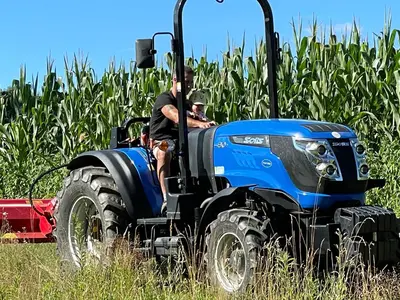 two men riding on a tractor in a cornfield at Boutique Glamping Divja DiVine in Zgornja Korena