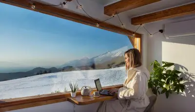 a woman sitting at a desk with a laptop in front of a window at Lunela estate with sauna in Cerklje na Gorenjskem