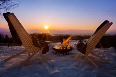 two chairs and a fire pit in the snow with the sunset at Lunela estate with sauna in Cerklje na Gorenjskem