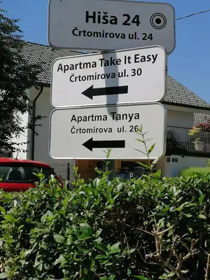 a street sign with three signs in front of a bush at Apartma Tanya Bled in Bled