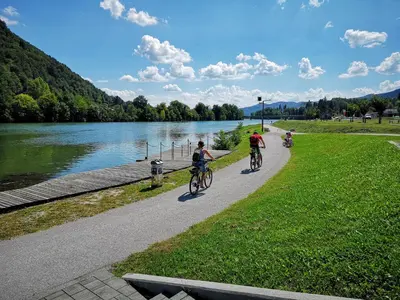 two people riding bikes down a path next to a river at Ribiška vasica - Fishermen's Village in Radeče
