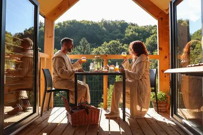a man and woman sitting at a table on a deck with drinks at Nesting Resort - Homestead SONČNI RAJ in Maribor