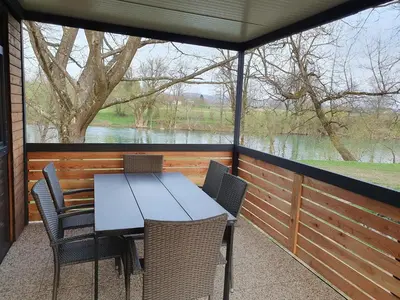 a table and chairs on a porch with a view of a river at GM House, mobile house near Kolpa river in Metlika