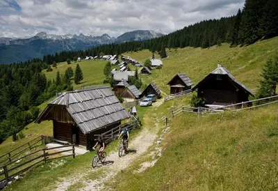 two people riding bikes in front of a mountain village at Villa Pokljuka in Zgornje Gorje