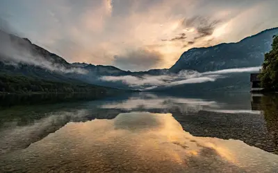 a body of water with a cloudy sky and mountains at V objemu gora in Bohinj