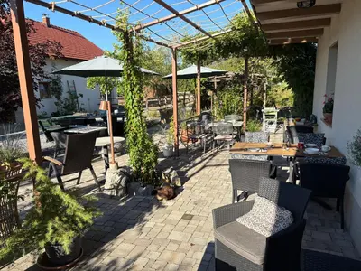 a patio with tables and chairs and a dog laying on the ground at Lipizzaner Lodge Guest House in Postojna