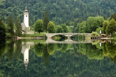 a bridge over a lake with a church and a clock tower at Accommodation Resman in Bohinj