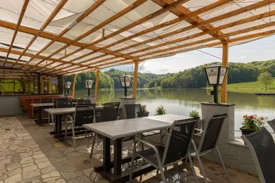 a patio with tables and chairs and a view of a lake at Penzion ob Ribniku in Podlehnik