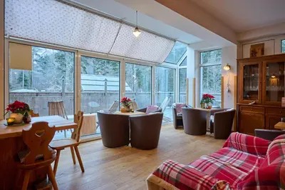 a living room with tables and chairs and windows at Eko hiša-Eco House Na razpotju in Solčava