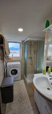 a bathroom with a shower and a sink and a washing machine at Apartma AJJA in Šenčur