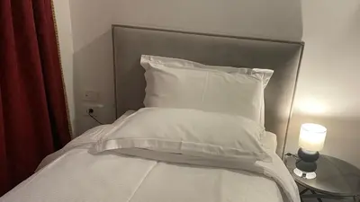 a bed with white sheets and a lamp on a table at MADONCA ROOMS & RESTAURANT in Nova Gorica