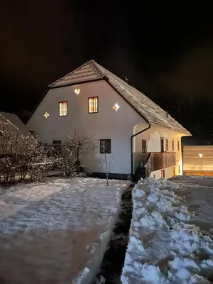 a house with lights on in the snow at night at Juvanova hiša (all house) in Luče