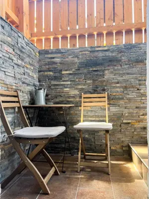 two chairs and a table in front of a stone wall at Lovely basement rental in Bled