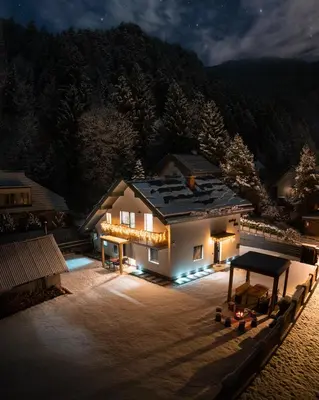 a large white house with lights in front of a mountain at Apartmaji ENIA Rateče-Planica, Kranjska Gora in Kranjska Gora