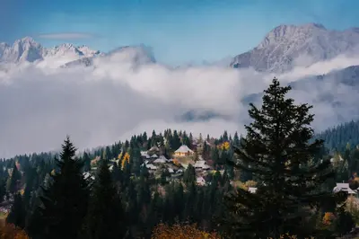 a town in the middle of a mountain with clouds at Koča Žafran - Velika planina in Stahovica
