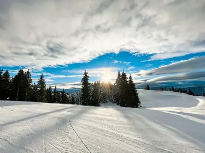 a snow covered slope with the sun in the sky at Sunshine Apartments Golte COMFORT in Mozirje
