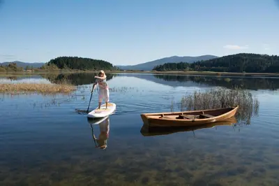a woman is standing on a paddle board on a lake at Apartment Lakeside Cerknica in Cerknica