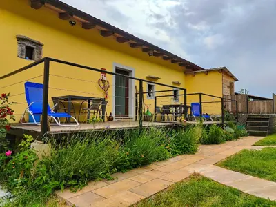 a yellow house with a deck with chairs and a table at Homestead Zavadlal - Domačija Zavadlal in Komen